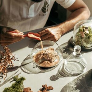 Close-up of a person creating a terrarium with sand, moss, and glass containers.